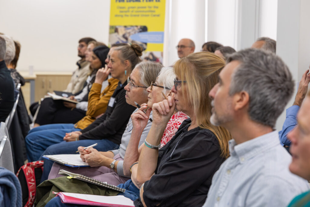 a group of people sit in an audience at an event listening to a speaker