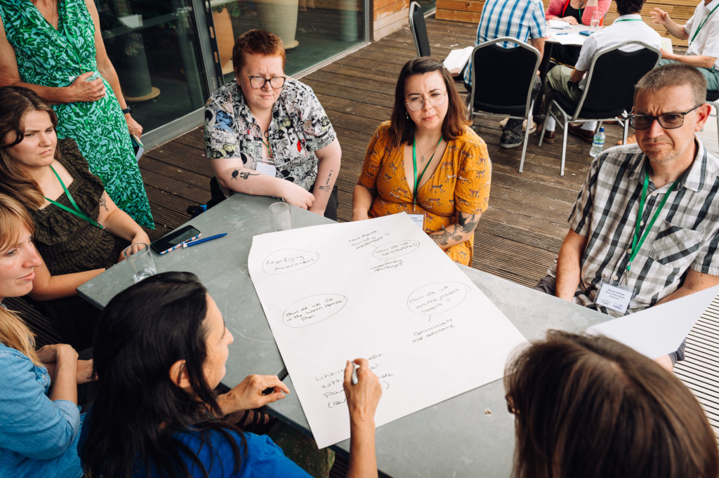 a group of people sit at a table around a flip chart on which someone is writing notes