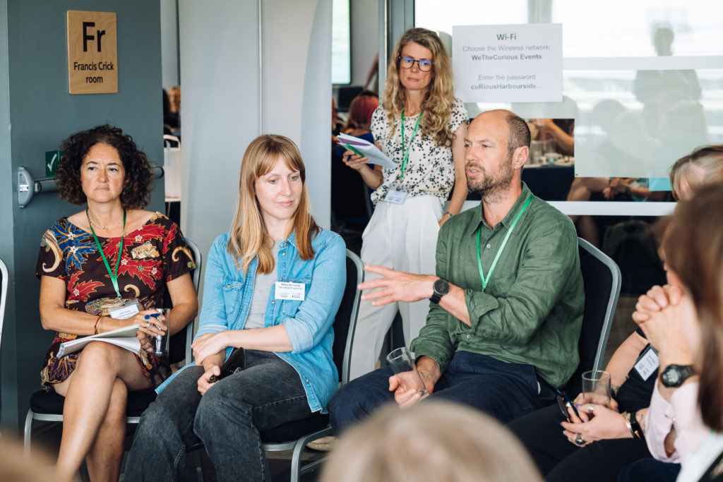 people sit in chairs in a circle, listening to one person speak