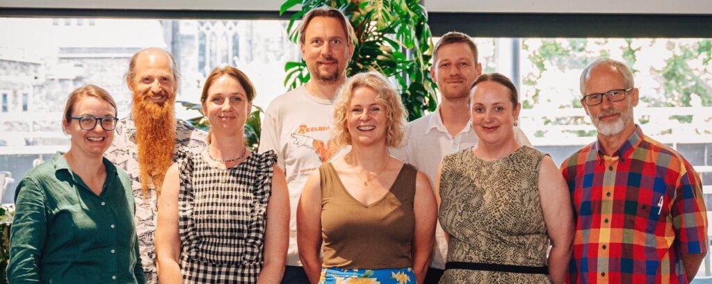 Eight smiling people stand together in a group photo