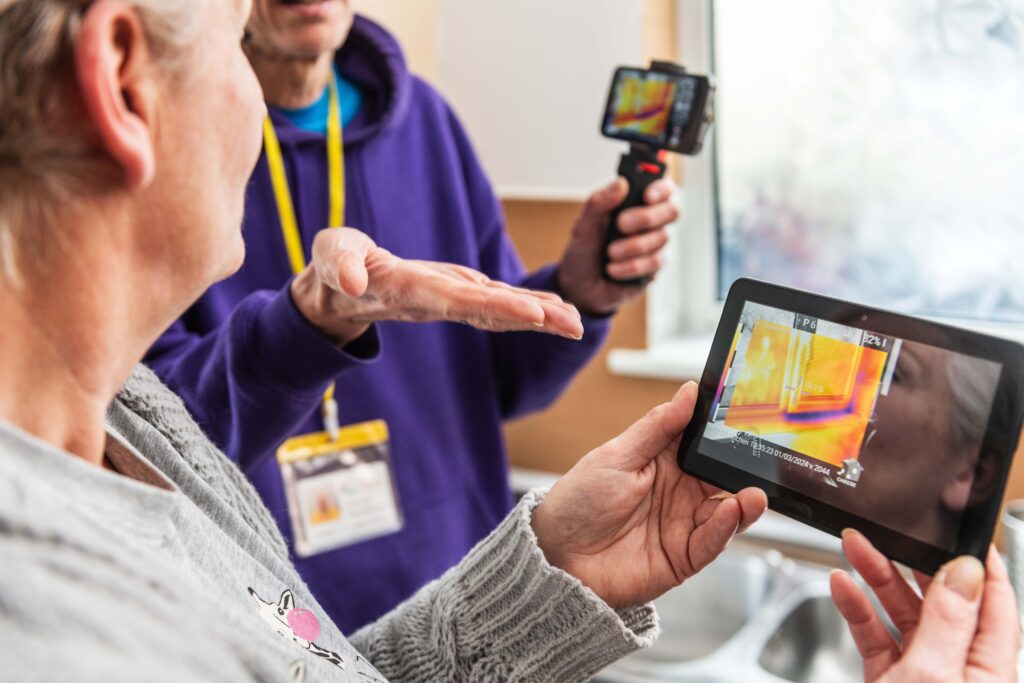 a person holds a screen with heat imaging on it while another person holding a camera gestures to it, palm up