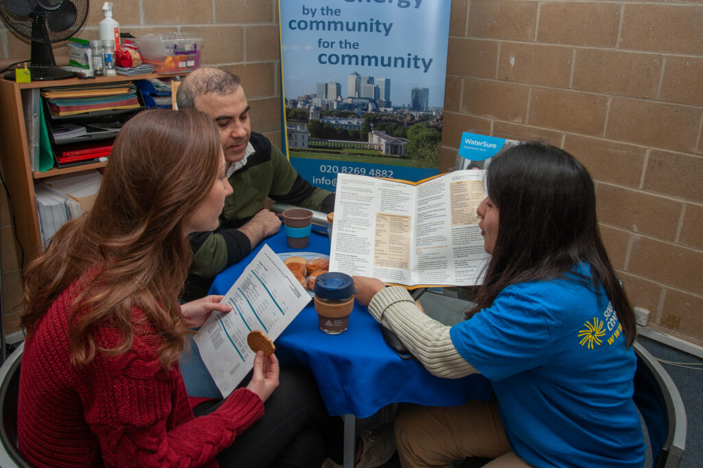 two people sit at a table listening to a person wearing a blue Selce t-shirt