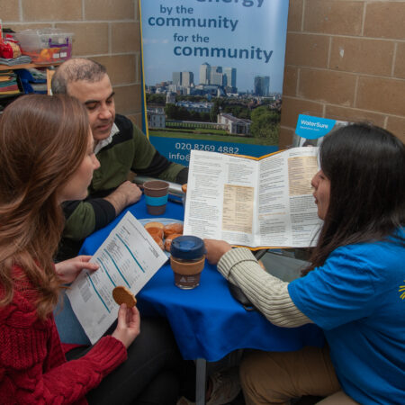 two people sit at a table listening to a person wearing a blue Selce t-shirt