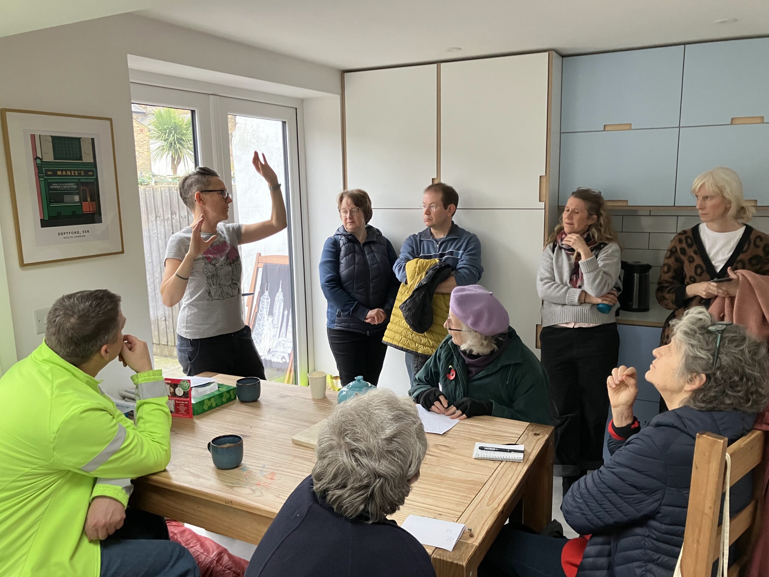 people stand and sit in a kitchen, listening to another person who is speaking and gesticulating
