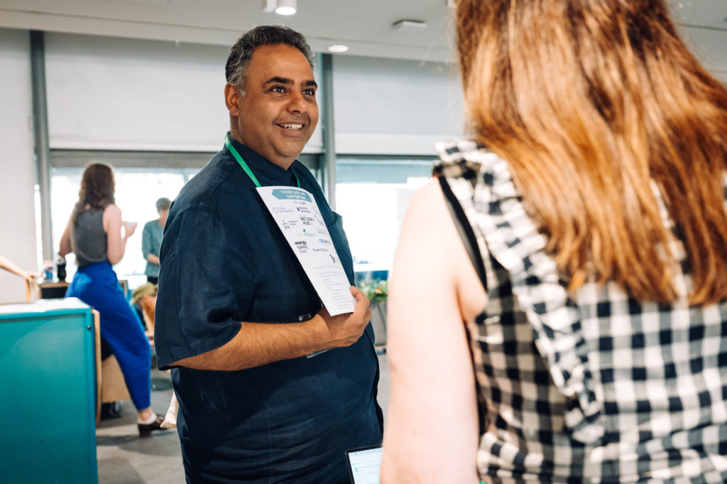 two people speak, one looking more directly towards the camera and the other with their back to the camera