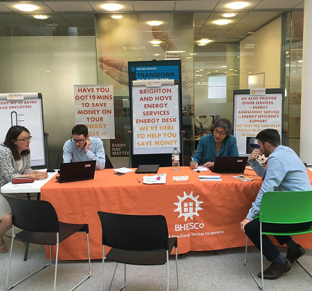 two pairs of people sit at a rectangular table with laptops and display stands