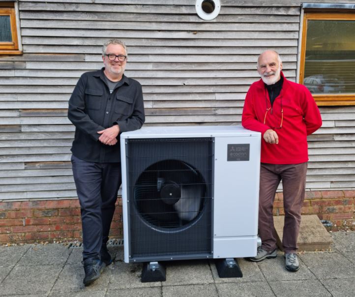 Two people stand on either side of an air source heat pump