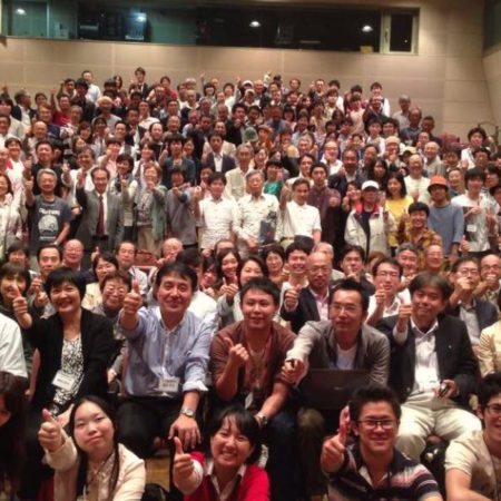 a large group of people smile at the camera, many of whom are holding thumbs up