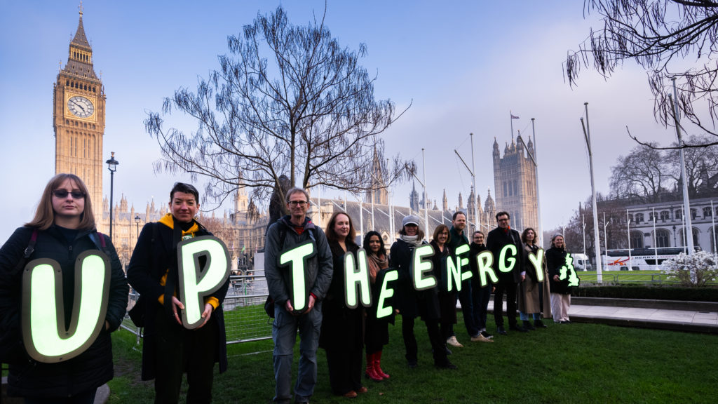 a group of people wearing letters spelling out 'Up the Energy' stand in front of Big Ben and whitehall