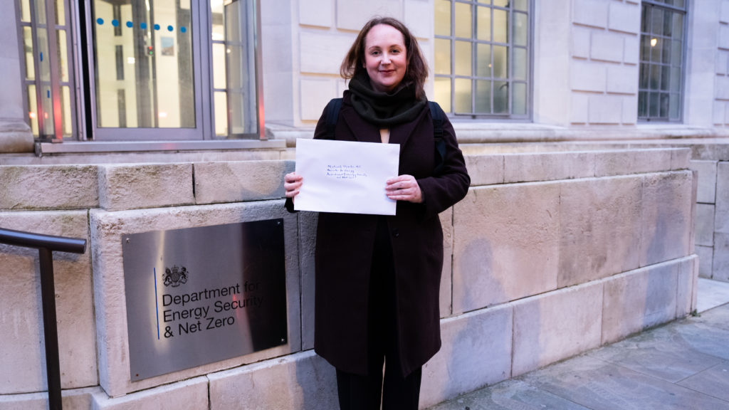 A person stands in front of a sign for Department of Energy Security and Net Zero holding a letter